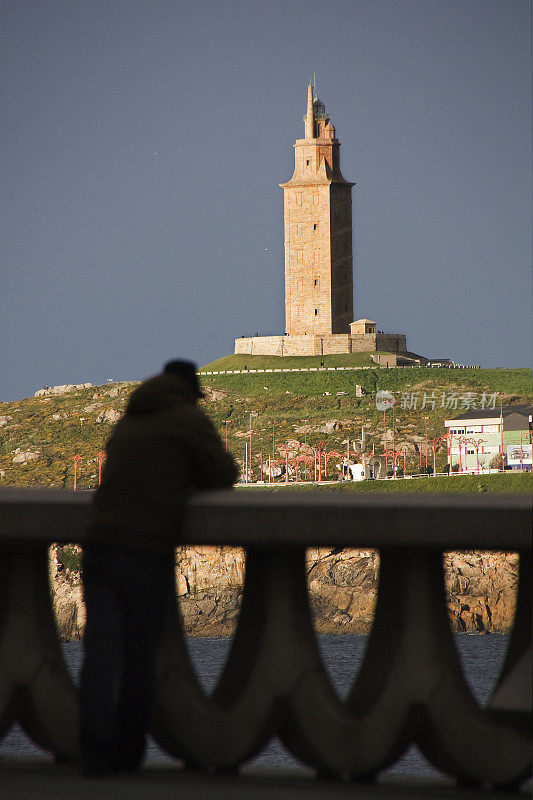 Torre de Hércules ancient lighthouse, unrecognizable person leaning on stone railing, looking at view. A Coruña city, Galicia, Spain.